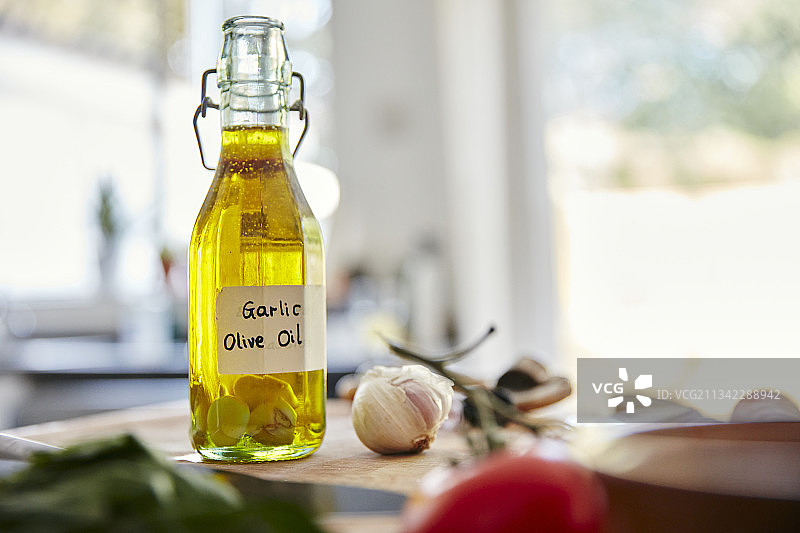 英国，家庭健康烹饪，厨房的切菜板上放着装着橄榄油和蒜瓣的玻璃瓶图片素材
