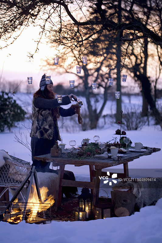 在白雪覆盖的花园里，女人把灯笼挂在树上，桌上摆着桌子图片素材