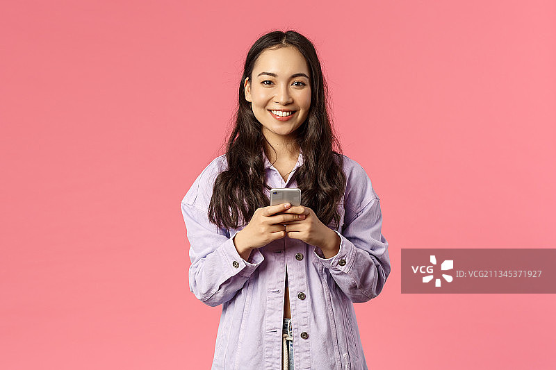 微笑的年轻女子肖像使用手机在粉红色的背景图片素材