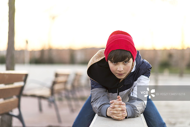 西班牙，巴塞罗那，格兰诺勒斯，一名戴着针织帽的时尚少年坐在城市公园的栅栏上图片素材