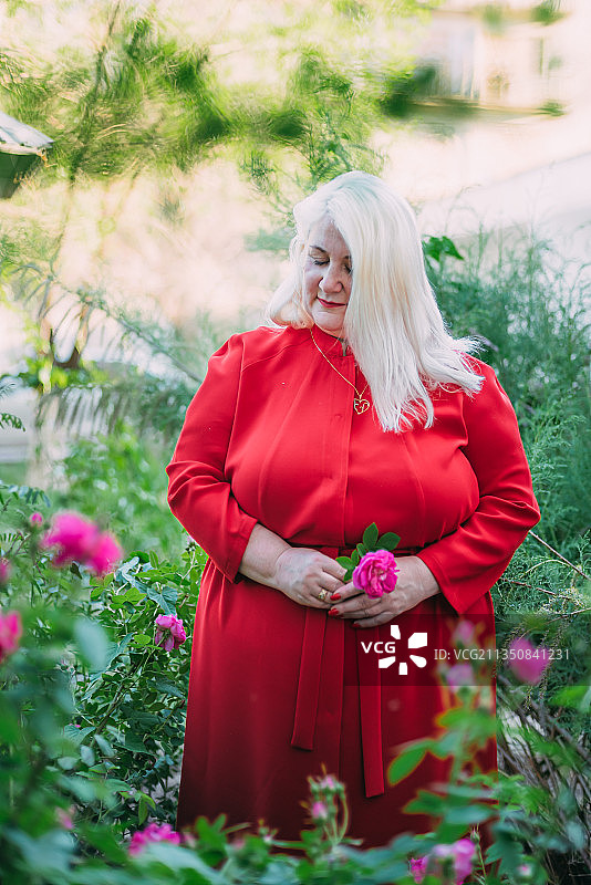 哈萨克斯坦，一名身穿红色连衣裙的女子站在户外的花园里图片素材