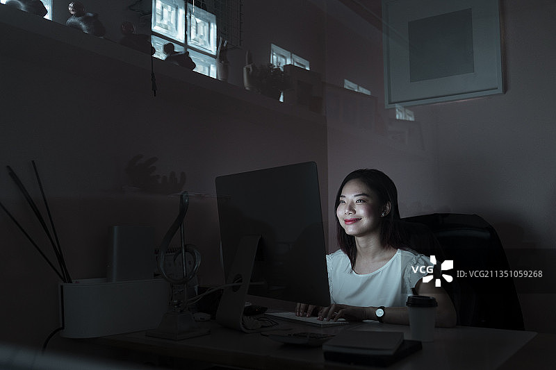 微笑年轻的亚洲女性对她的工作结果感到满意，工作到深夜-加班。图片素材