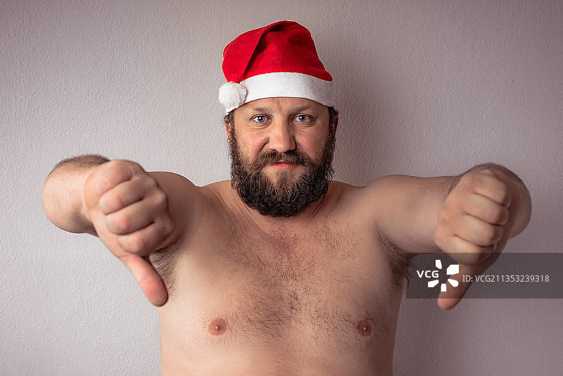 男人的肖像戴着圣诞老人的帽子在灰色的背景下做手势图片素材
