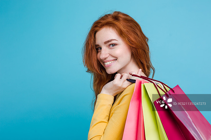 一个带着购物袋微笑的年轻女子的肖像站在蓝色的背景下图片素材