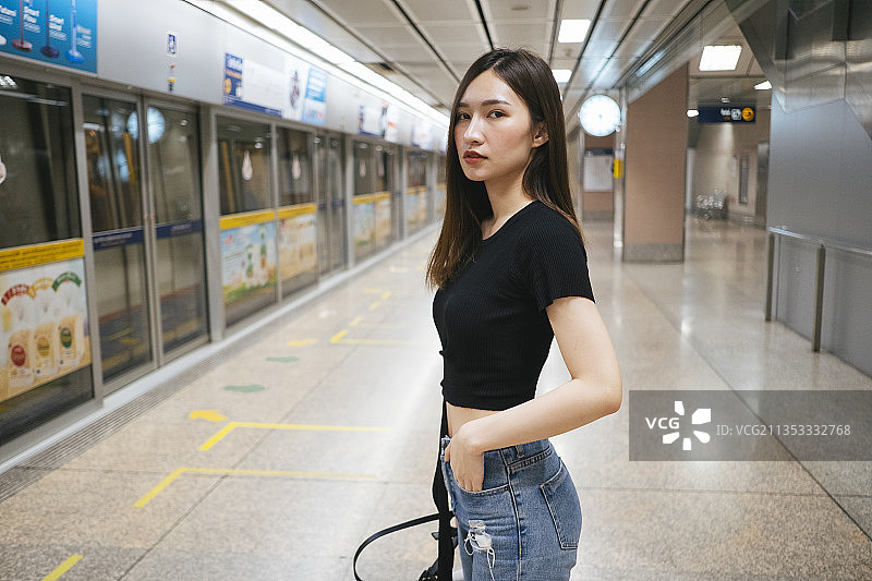时尚肖像-年轻的亚洲泰国妇女在黑色衬衫和牛仔裤裤子等待在地铁站站台的火车。图片素材