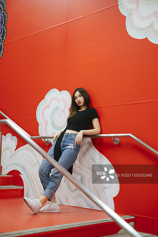 时尚肖像-年轻的亚洲泰国妇女在黑色衬衫和牛仔裤裤子摆姿势在红色楼梯涂鸦。图片素材