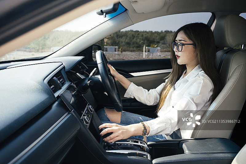 交通和车辆概念——泰国女子身穿白衬衫，戴着眼镜在车内开关齿轮旋钮。图片素材