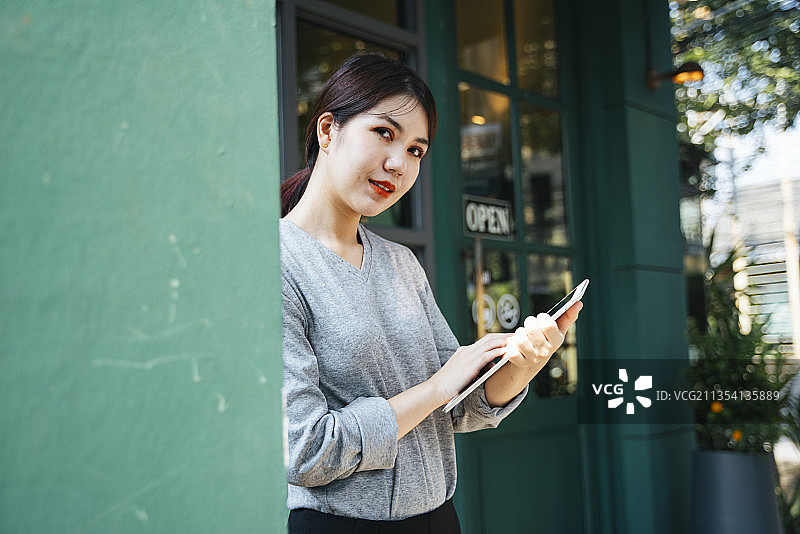 漂亮的年轻亚洲女人使用平板电脑在街上的咖啡馆背景。图片素材