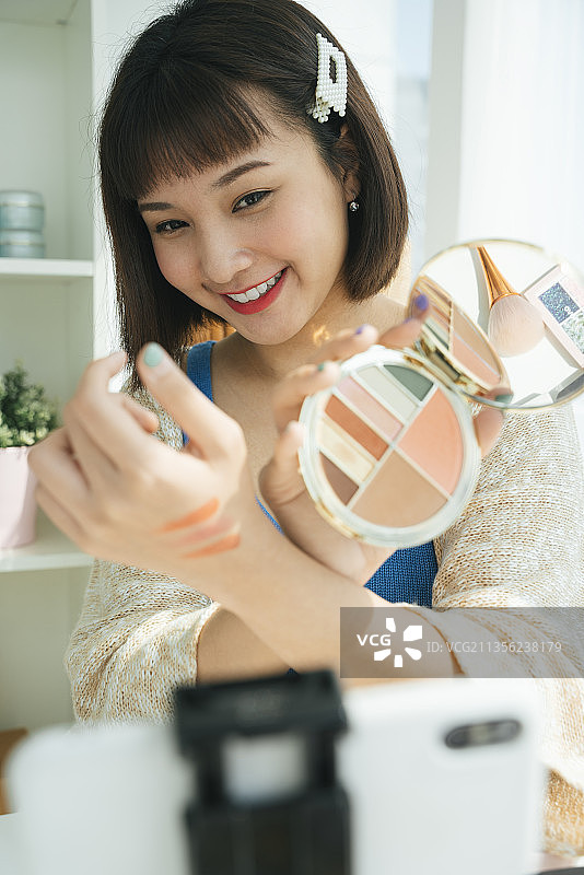 美丽年轻的亚洲美容博主评论化妆品直播与智能手机。网红女孩社交媒体营销直播智能手机概念。图片素材