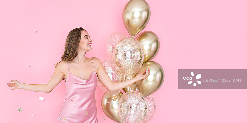 拿着气球站在粉红色背景下的女人图片素材