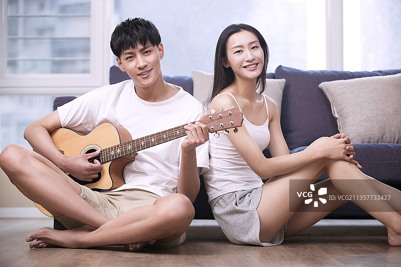 年轻男子在客厅为女朋友弹奏吉他图片素材