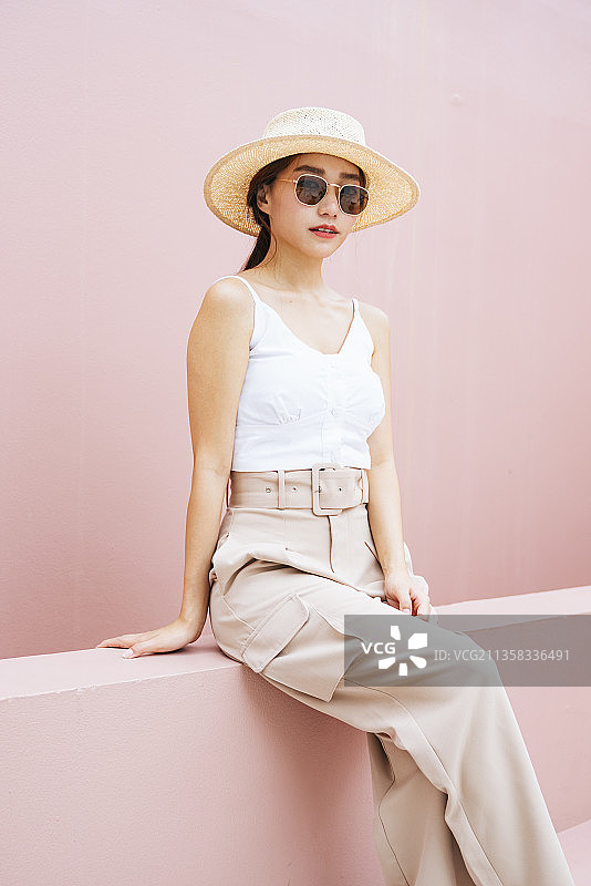 美丽的年轻亚洲女人的肖像戴着帽子和太阳镜孤立在粉红色的背景。图片素材
