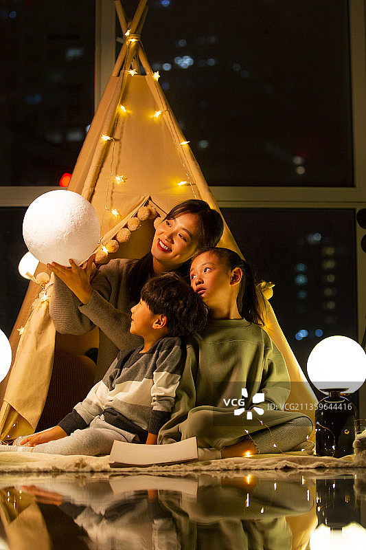 妈妈、女儿和儿子在客厅露营拿着月球灯玩耍图片素材
