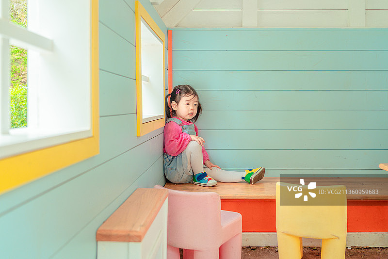 坐在蓝色小木屋窗户角落处休息的小女孩图片素材