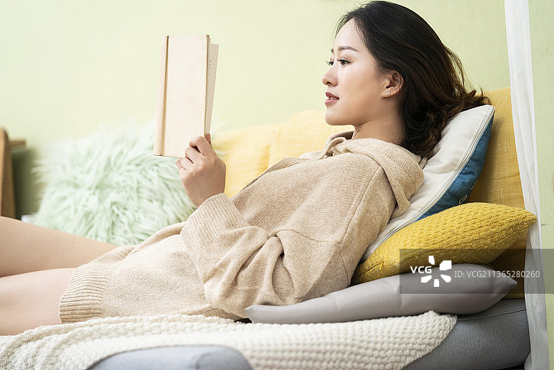 年轻女士躺在沙发上看书图片素材
