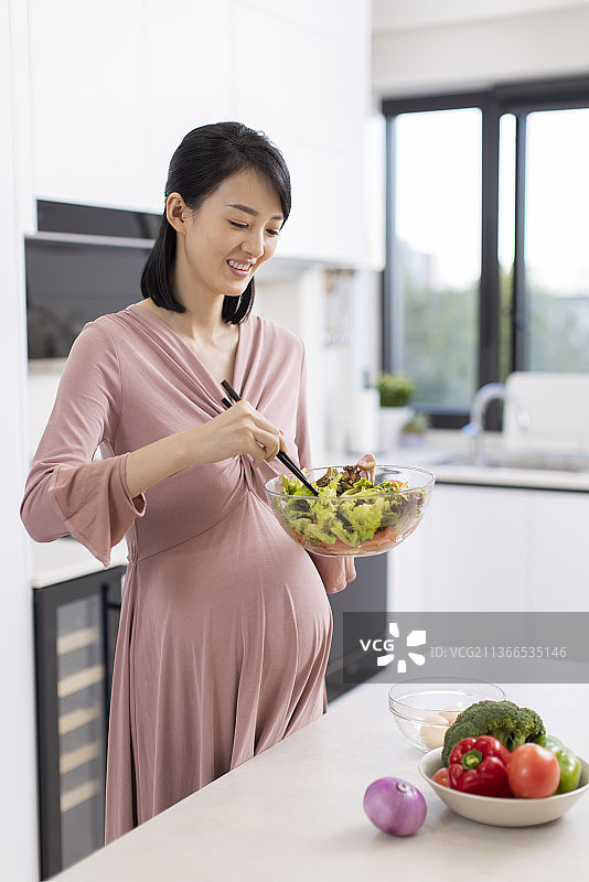 快乐的年轻孕妇在家做饭图片素材