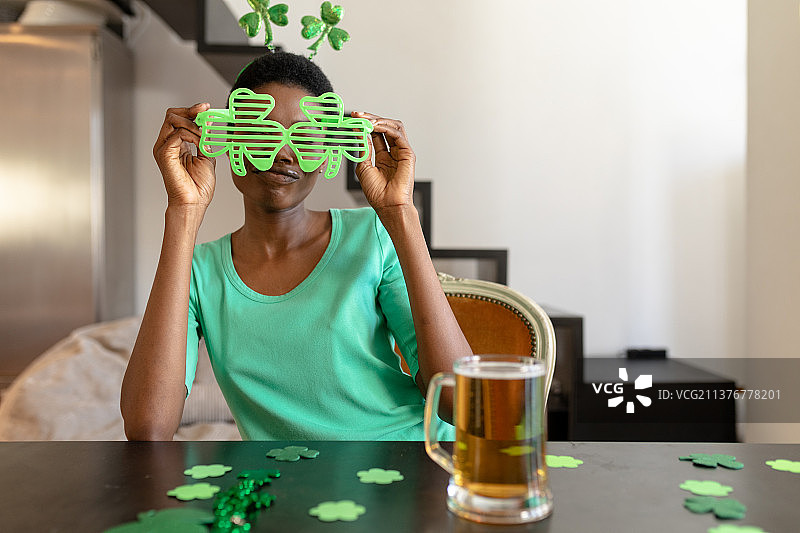 非洲裔美国妇女拿着三叶草新奇的玻璃杯，而坐在桌子的啤酒杯图片素材