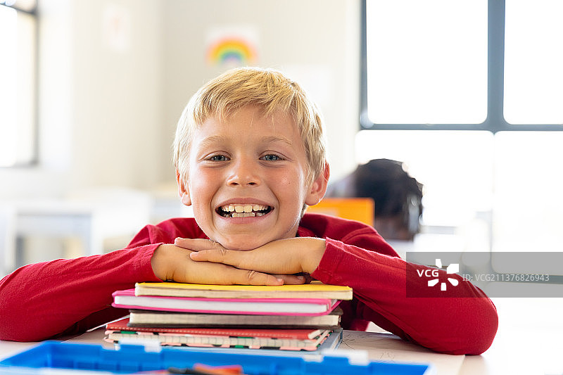 在教室里，一名白人小学生靠在课桌上，面带微笑图片素材