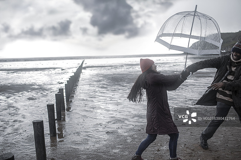 在潮湿的冬季海滩上，一对带伞的情侣图片素材