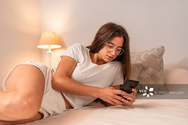 年轻的拉丁女人拿着手机躺在床上图片素材