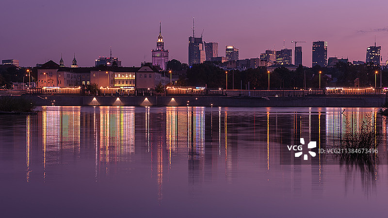 城市灯光，景观照明的建筑物由河对天空在晚上，华沙，波兰图片素材