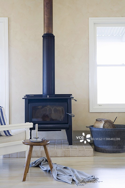 在一间明亮而简洁的客厅里，在凸起的石头平台上，有一个铸铁火炉，前面放着一张复古的木凳图片素材