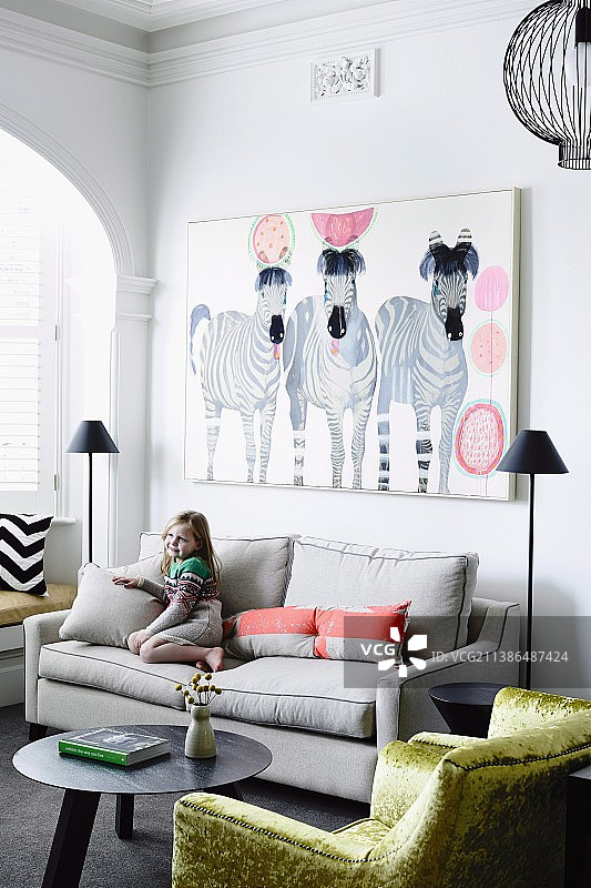 小女孩在沙发下面画着斑马和金光闪闪的天鹅绒扶手椅图片素材