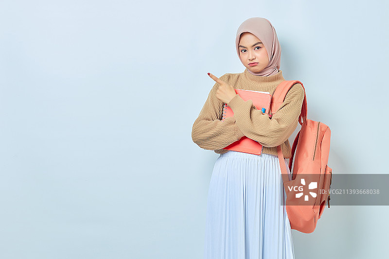 身穿棕色毛衣、背双肩包的年轻亚洲穆斯林女学生沉思着，手指放在一边图片素材