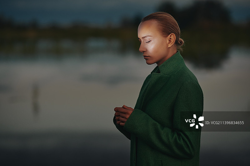 美丽女人的肖像，穿着绿色的外套，旁边的池塘。黄昏日落的光线。很适合做书的封面图片素材