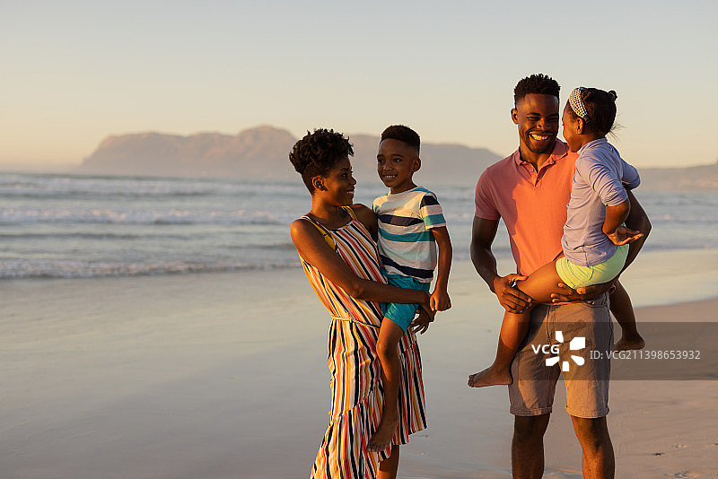 快乐的非洲裔美国年轻父母抱着儿子和女儿站在大海和天空图片素材