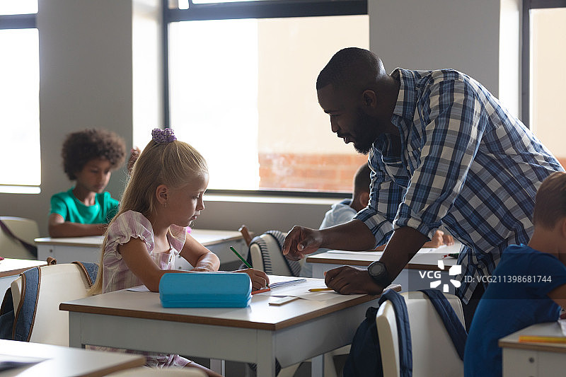 非洲裔美国年轻男性教师在教白人小学生坐在课桌前图片素材