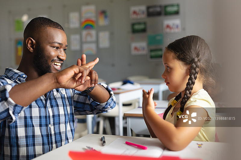 微笑的非洲裔美国年轻男性教师教白人小学女孩手语图片素材