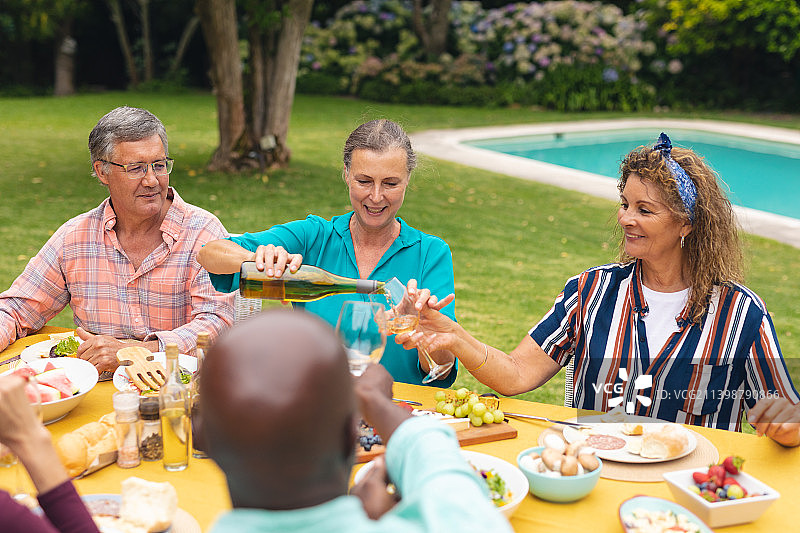 多种族的老年男性和女性朋友在餐桌上喝酒在后院聚会图片素材