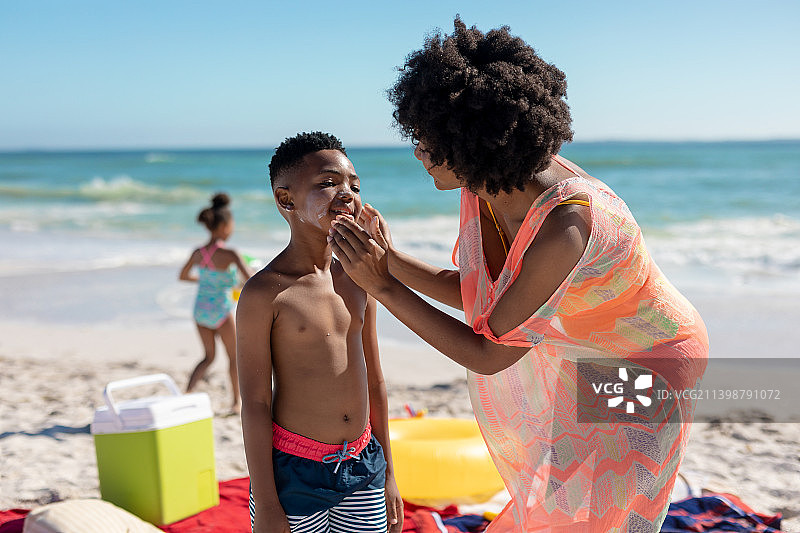 非洲裔美国妇女在阳光明媚的日子在海滩上给儿子的脸颊涂防晒霜图片素材
