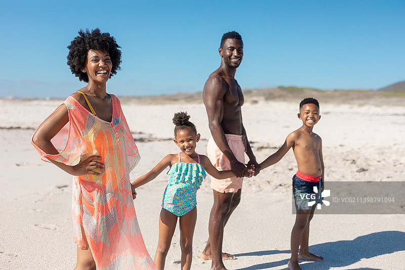 幸福的非裔美国家庭的肖像，手牵着手，而站在海滩上的晴天图片素材