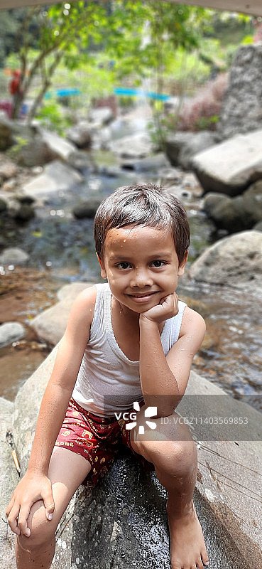 微笑的男孩坐在小溪中的岩石上的画像图片素材