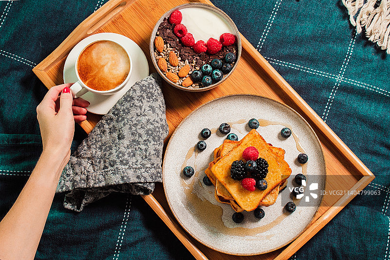 早餐放在床上，女人的手，酸奶碗和浆果，法式吐司图片素材