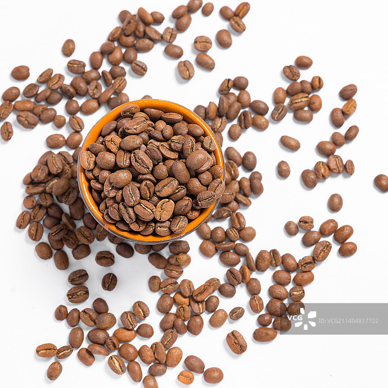 散落在白色照片上的咖啡豆和一个装有咖啡豆的马克杯图片素材