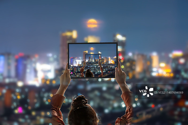 城市夜晚光斑光影中的一双女人的手举起相框框起现代城市摩天大楼与圆月图片素材