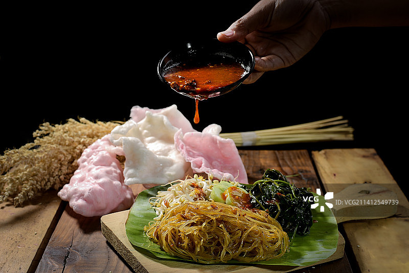 在印度尼西亚西爪哇的Cirebon，黑色背景下，裁剪过的手将酱汁倒在食物上图片素材