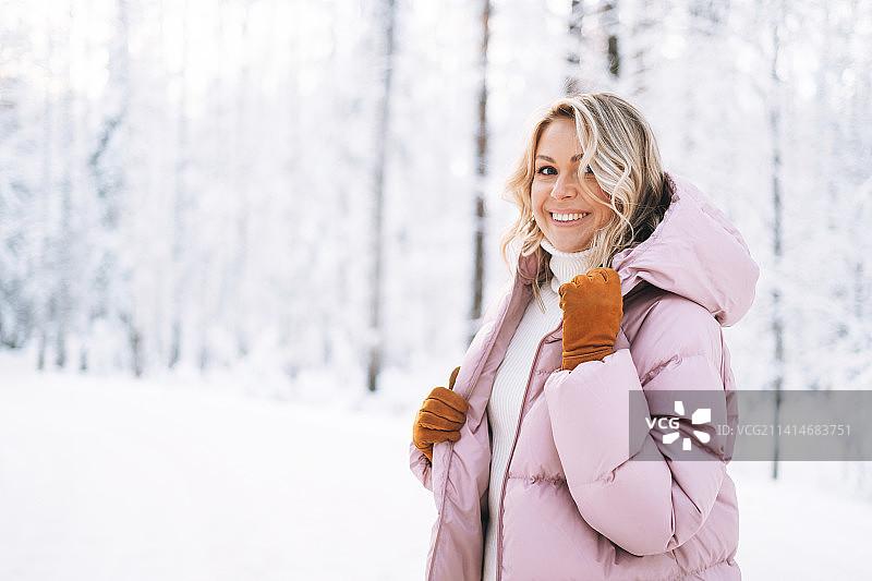 俄罗斯斯维尔德洛夫斯克州叶卡捷琳堡，白雪覆盖的冬季森林里，身着冬装的金发微笑女子的肖像图片素材
