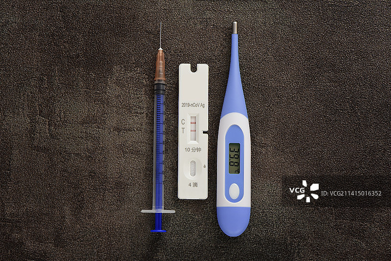 深色压抑背景上显示阳性的核酸检测抗原检测试剂和注射器体温计图片素材