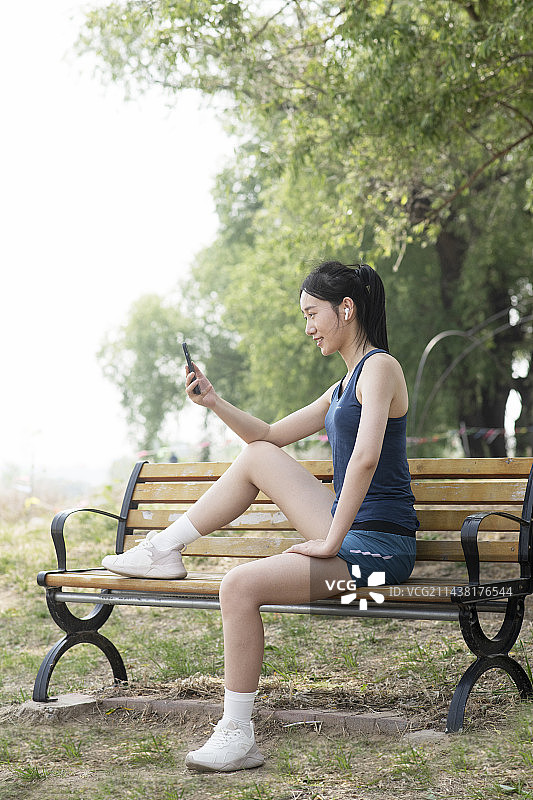 年轻女子在公园长椅上用智能手机图片素材