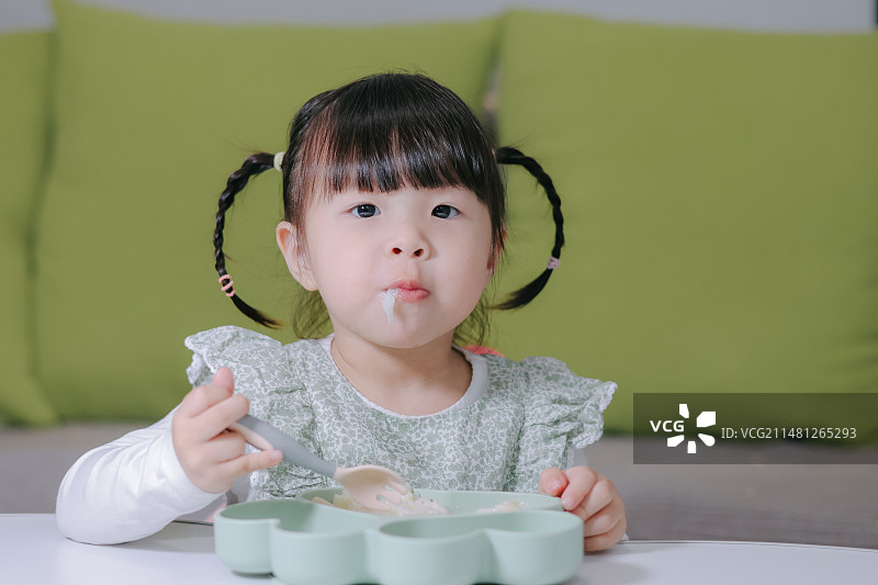 一位身穿绿色碎花裙的亚洲小女孩 独自吃饭图片素材