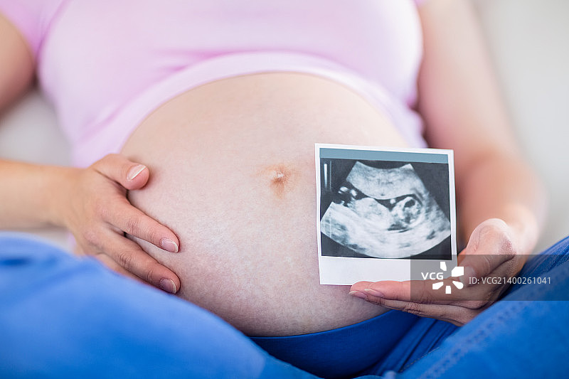 一名孕妇在客厅里展示超声波扫描并触摸自己的腹部图片素材