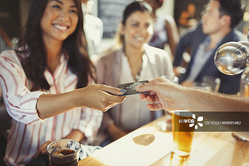 一个微笑的女人在酒吧用信用卡给酒保付钱图片素材