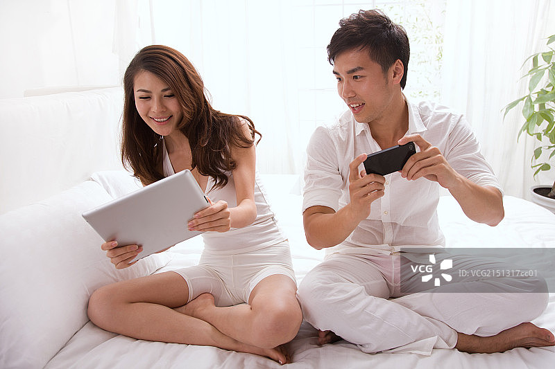 年轻夫妇坐在床上看平板电脑图片素材