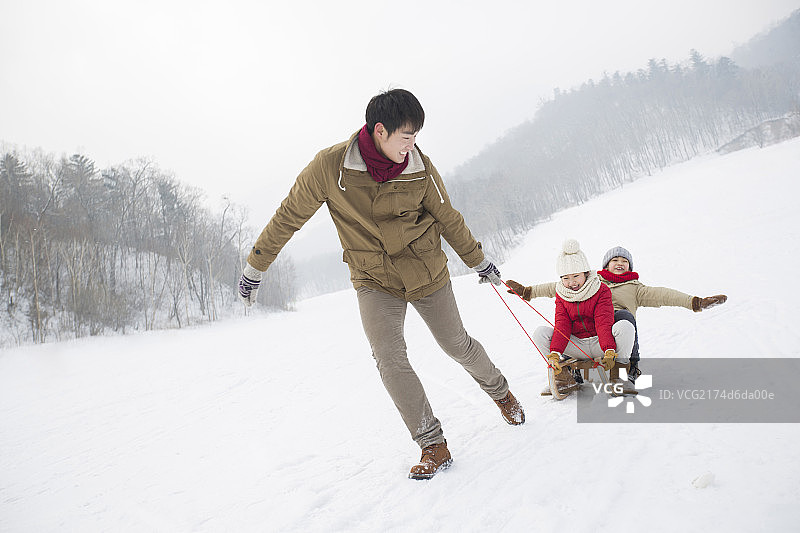 年轻的父亲和儿女在雪地上玩雪橇图片素材