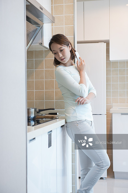Young woman using mobile in kitchen图片素材
