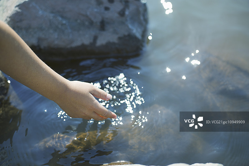 一个小女孩俯身将手伸进清澈浅浅的湖水中。图片素材